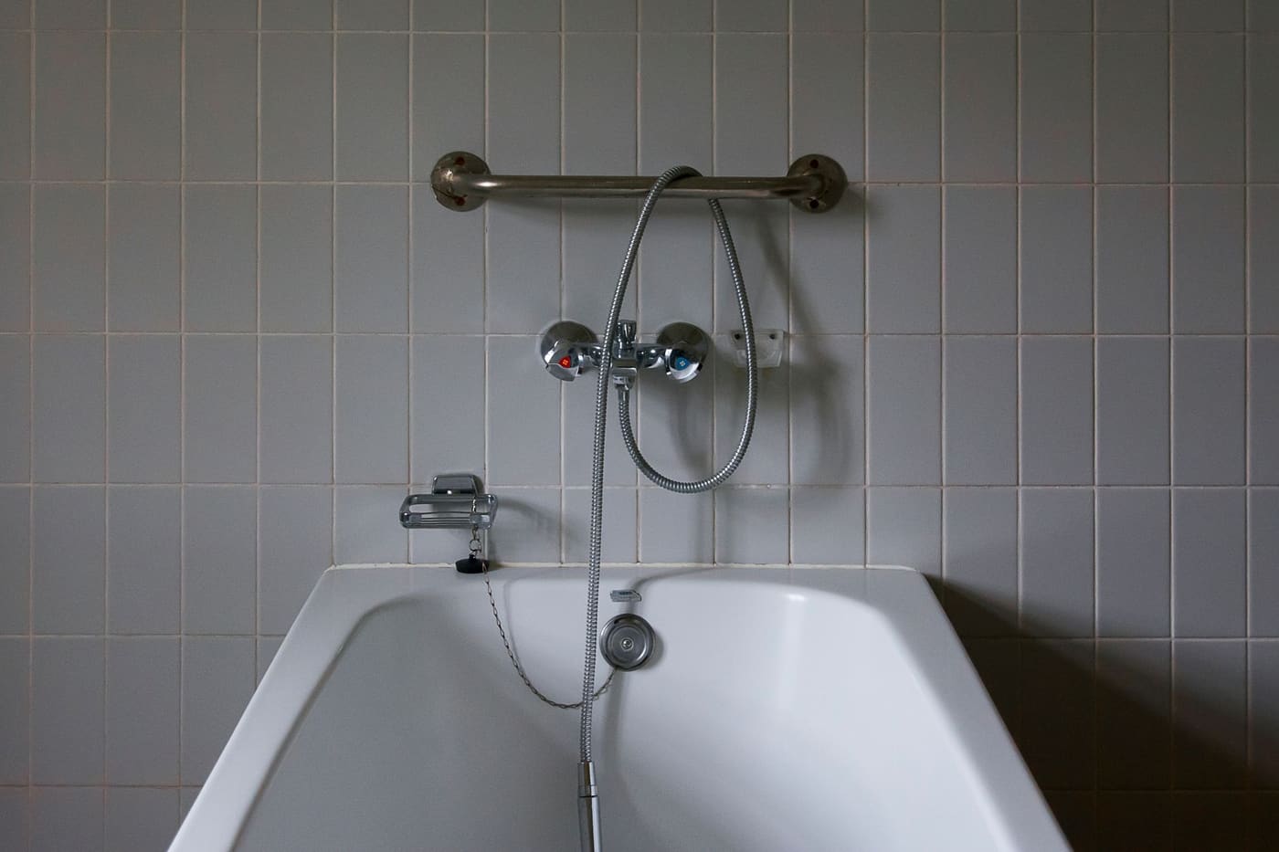 A bathtub with a metal grab bar fixed to the tiled wall above the taps