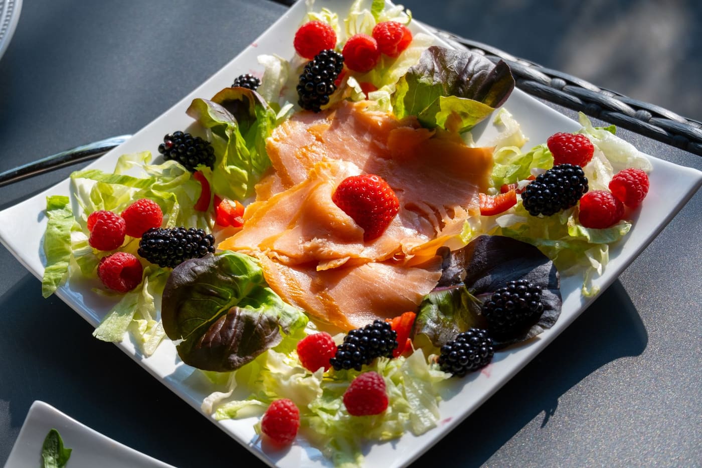 A plate of smoked salmon on salad leaves with raspberries and blackberries